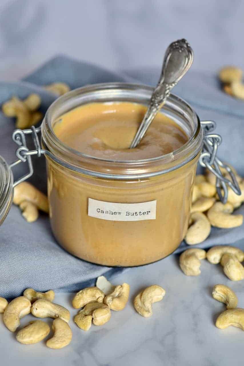 Homemade cashew butter in a jar with a spoon and a few cashews around 