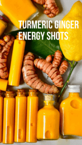 7 small glass vials filled with turmeric and lemon shots laying on a flat surface with some turmeric roots and a whole lemon with a leaf