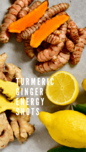 A small pile of turmeric root, a small pile of ginger root and one whole and one half lemon on a gray flat surface