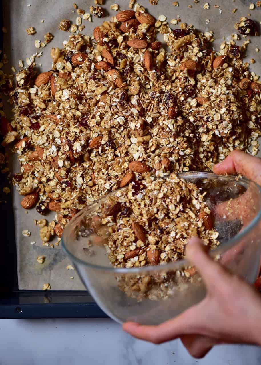 pouring granola mix over a baking tray 