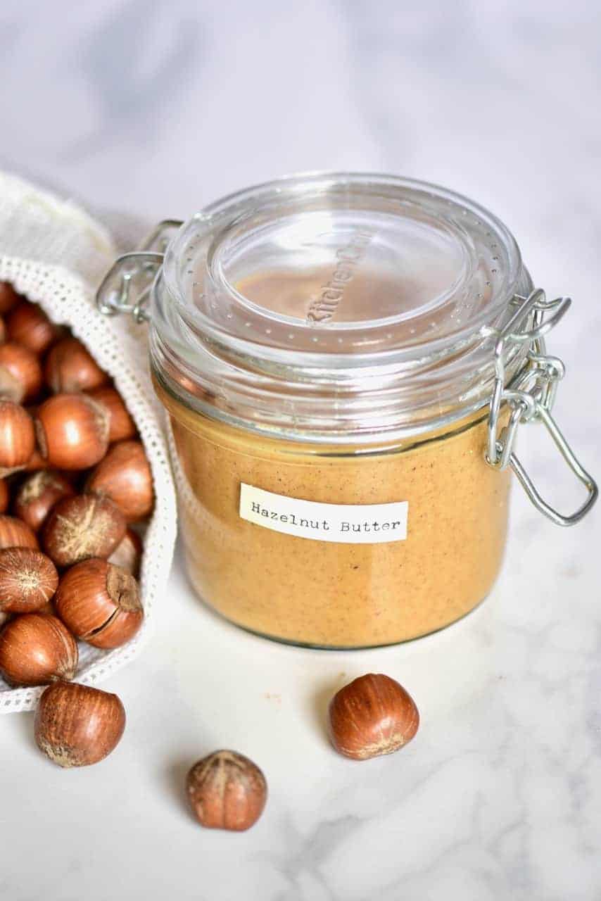 Homemade hazelnut butter in a jar and some hazelnuts next to it