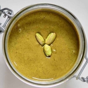 Top view of pistachio butter and three pistachios in a jar