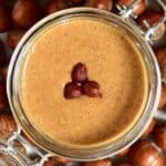 Top view of hazelnut butter and three hazelnuts in a jar and hazelnuts around it on a flat surface - 18