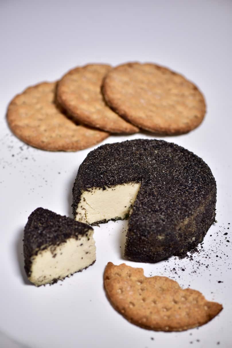 Homemade cashew cheese round with a cut slice and some crackers behind it