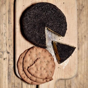 Homemade cashew cheese round with a slice cut off and a few crackers on a wooden board