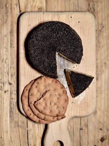 Homemade cashew cheese round with a slice cut off and a few crackers on a wooden board