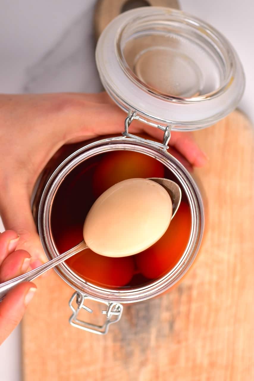 A ramen egg in a spoon over a jar with marinade