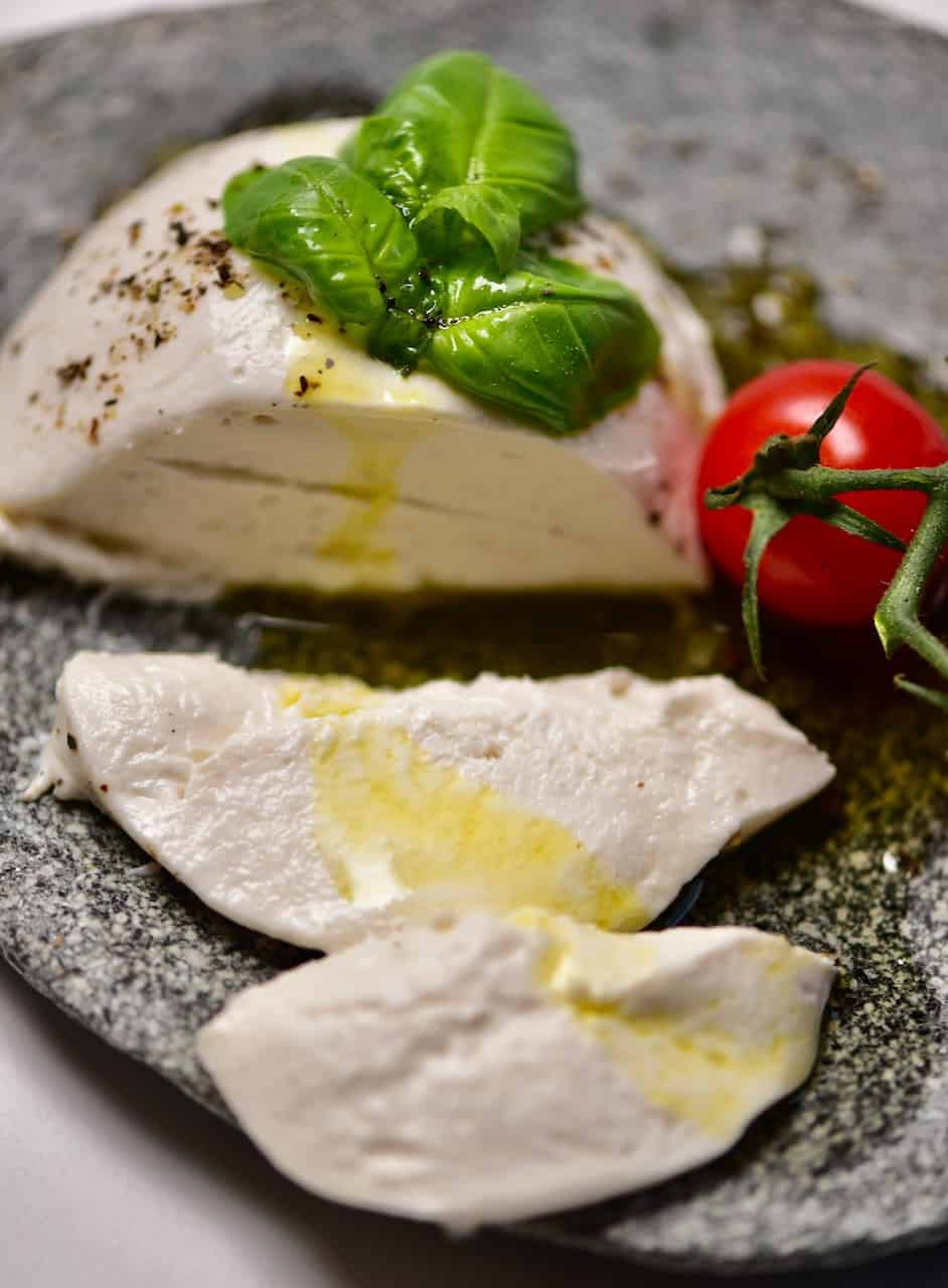 A simple stretchy, gooey and delicious vegan mozzarella on a plate with a cherry tomato and basil leaf