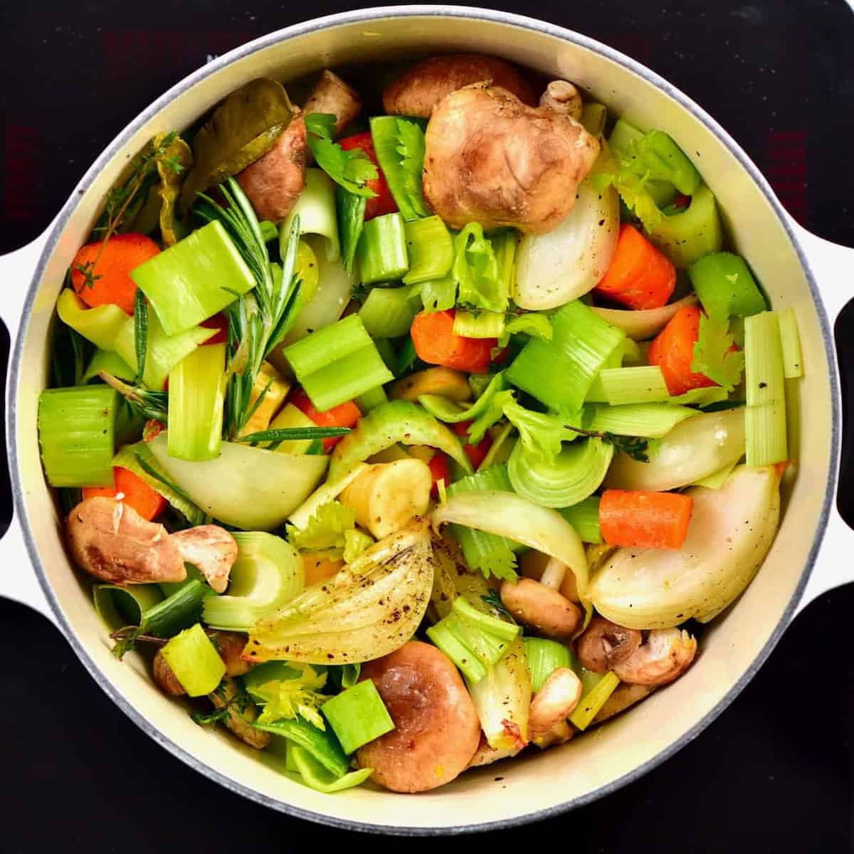the ingredients for a delicious homemade vegetable stock including carrots, parsnips, mushrooms, celery, onion, garlic, ginger and a variety of herbs