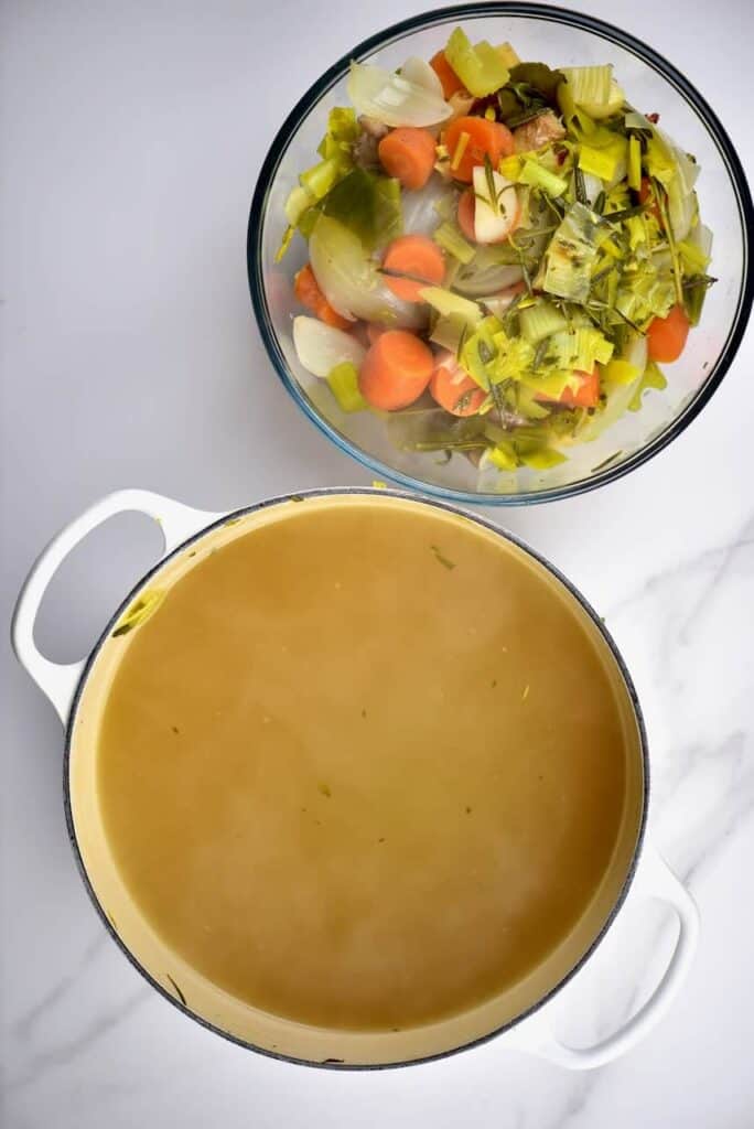A bowl of boiled vegetables and a pot of vegetable stock