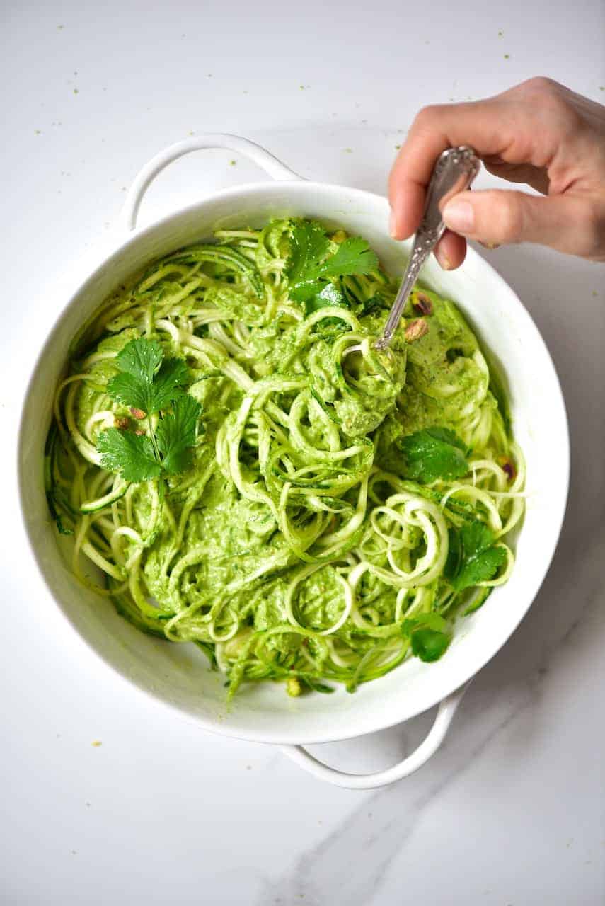 A hand with a fork with Zoodles with Pistachio pesto