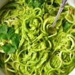 A close up of a bowl of noodles with pesto and a fork