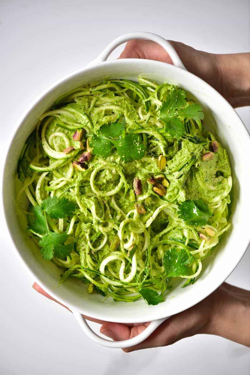 Two hands holding a dish with Zoodles and Pistachio pesto