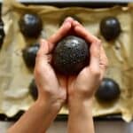 A black burger bun being held in hands over a tray with more black burger buns - 16