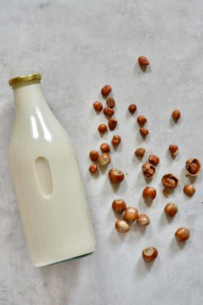 A bottle of hazelnut milk with some nuts on the side