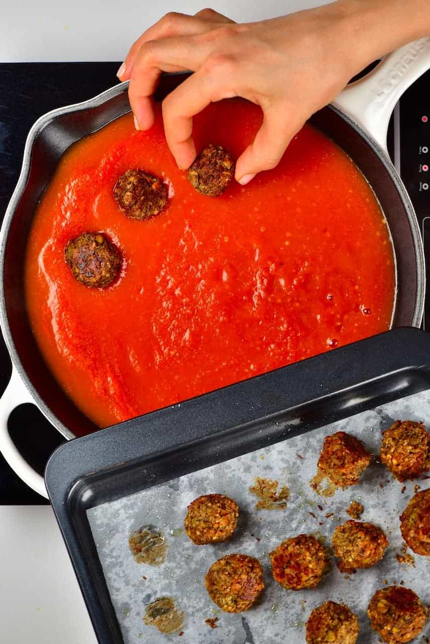 Arranging lentil meatballs in tomato sauce