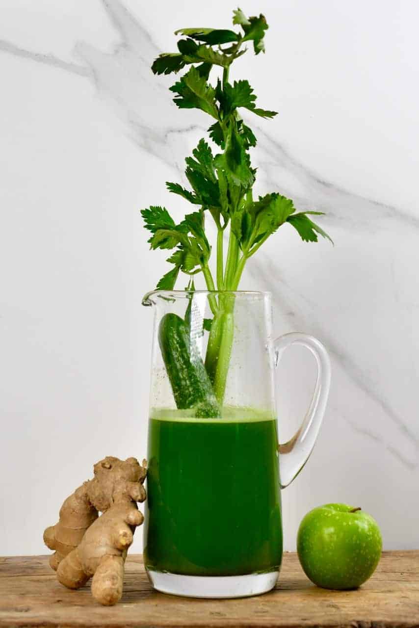 Celery Juice in a pitcher with apple and ginger next to it