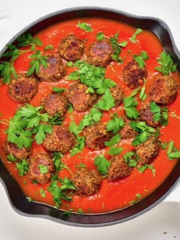 A large pan with mushroom and lentil vegan meatballs and tomato sauce topped with parsley