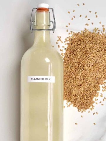 Flax Milk in a glass bottle and some flaxseeds next to it on a flat surface