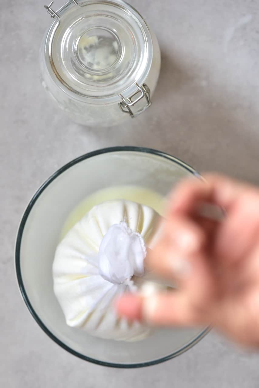 straining yogurt over a bowl, through a nut milk bag