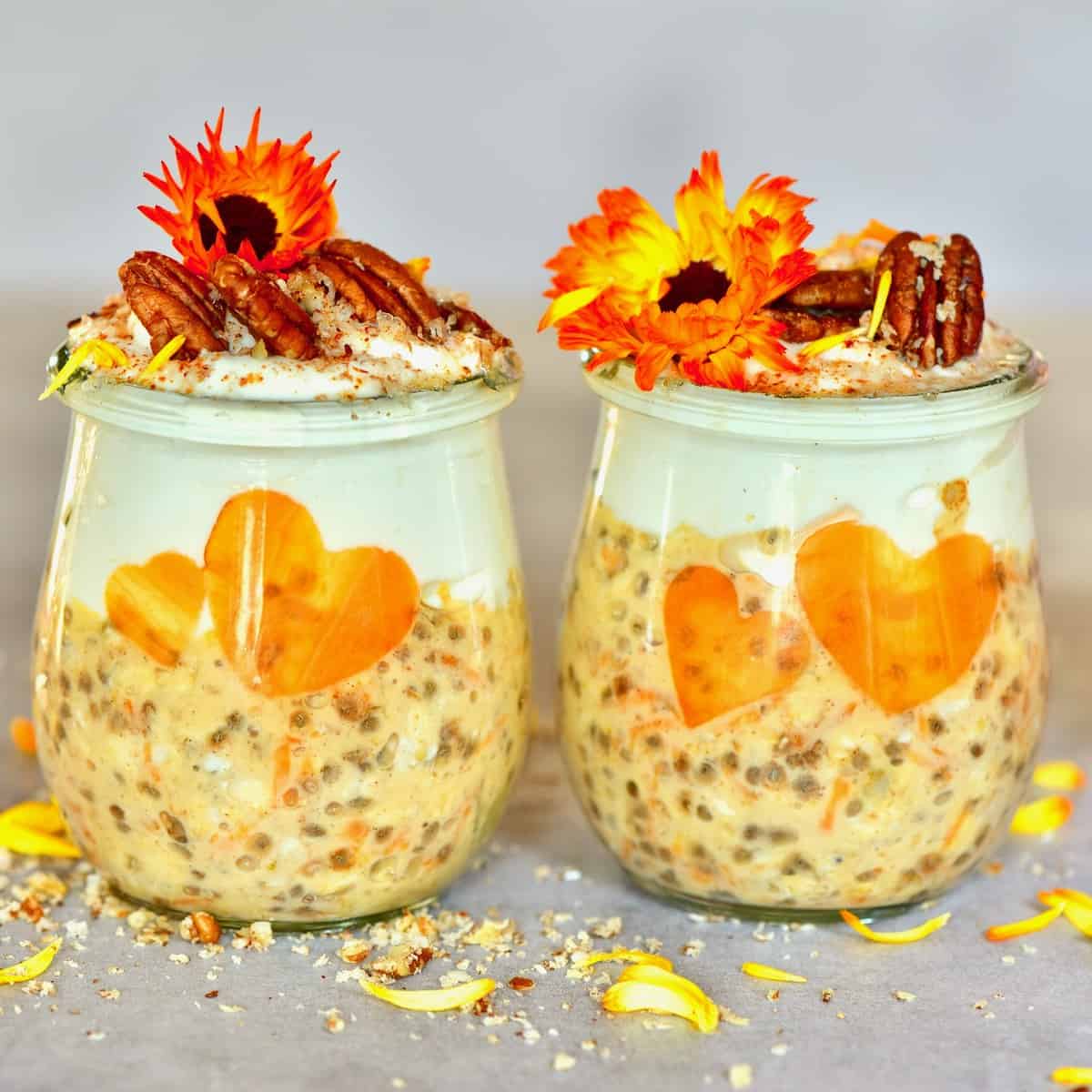 Two jars of carrot cake overnight oats decorated with pecans and edible flowers square