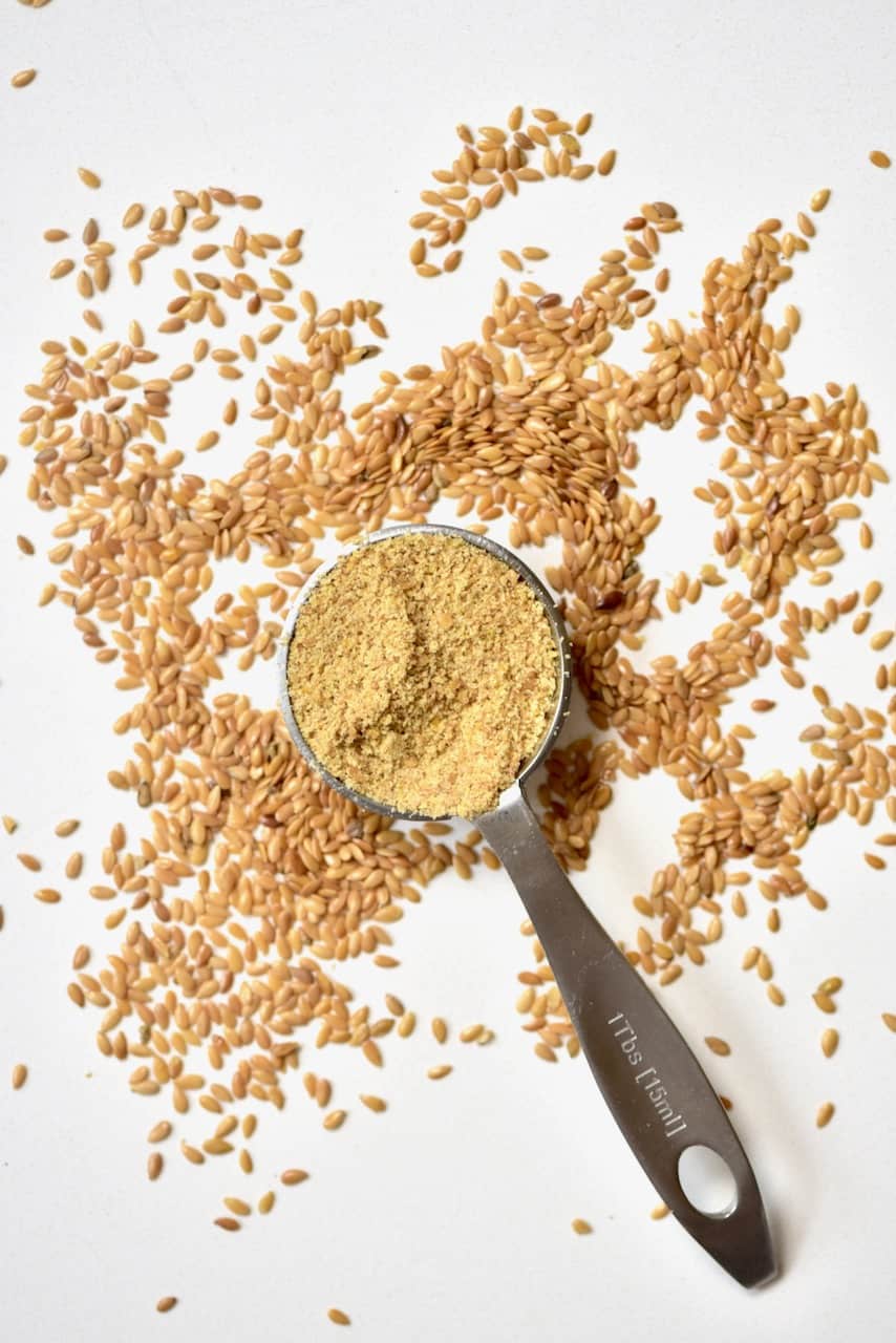 Tablespoon of ground Flaxseed next to unground flaxeed