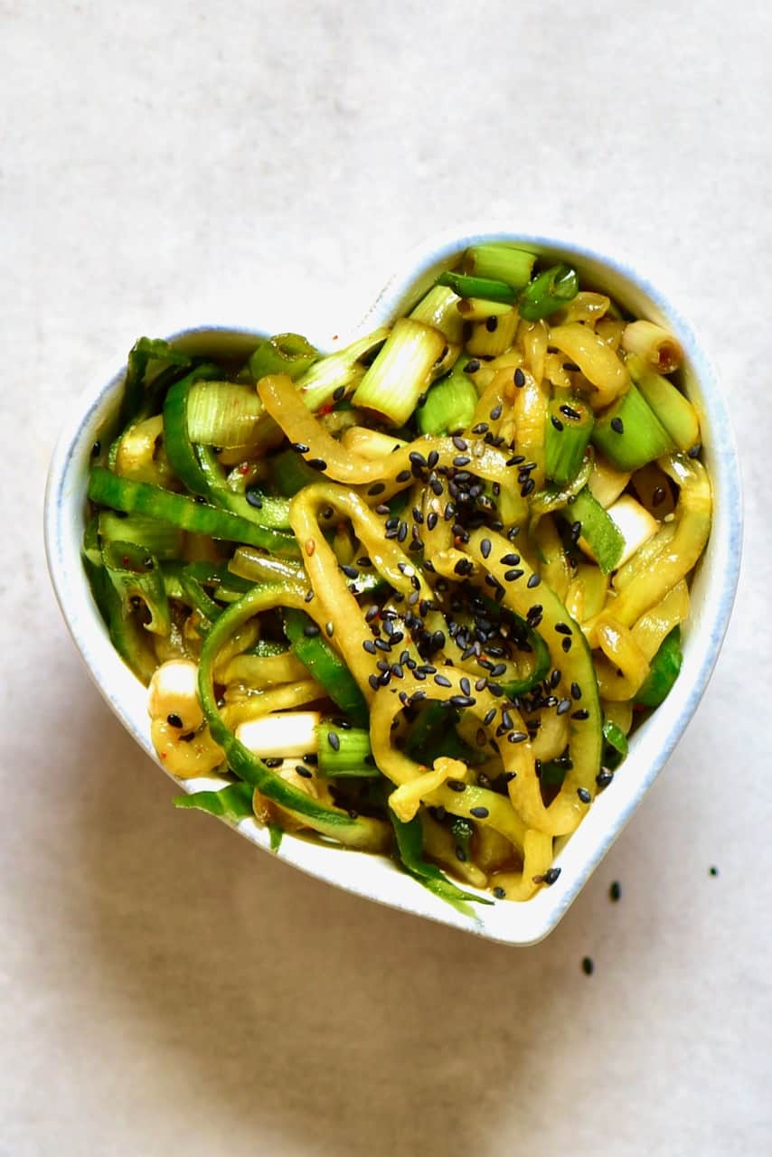 asian cucumber salad in a heart shaped bowl topped with black sesame
