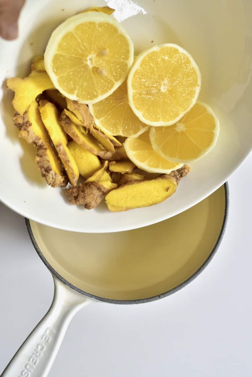 adding ginger and lemon slices to saucepan with water
