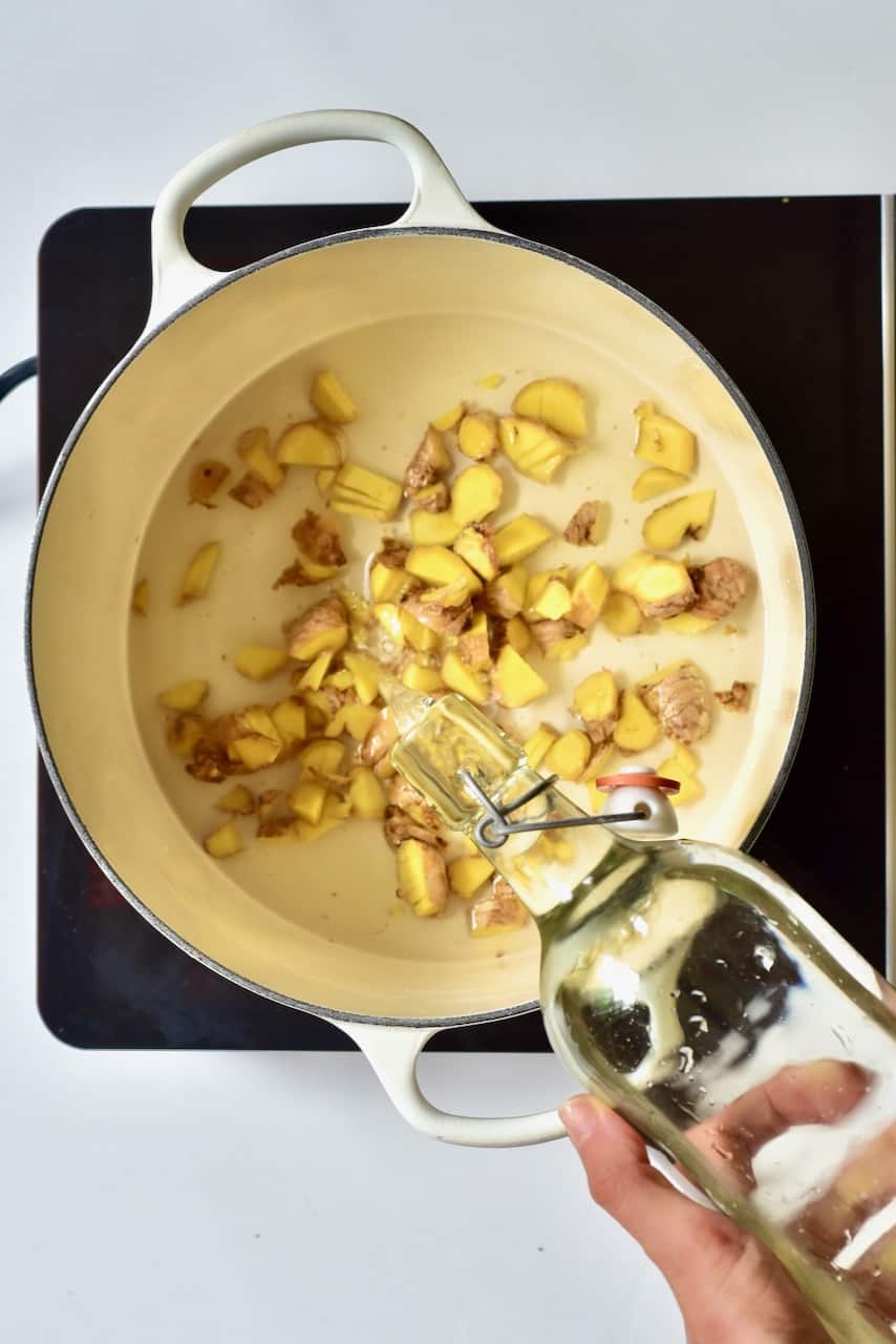 pouring water on chopped ginger in a white pot