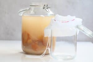 A big jar with homemade apple cider vinegar and a small jar with a nut milk bag
