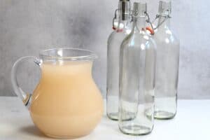 A jug filled with homemade apple cider vinegar and three empty bottles