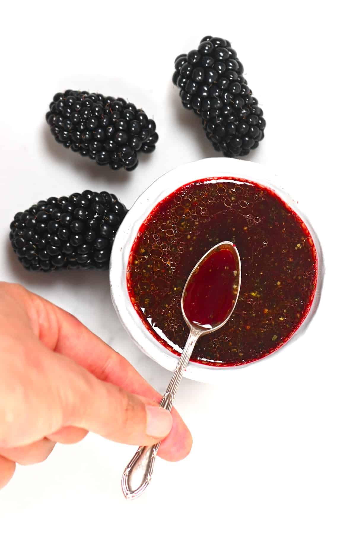 A spoon with blackberry salad dressing over a small bowl