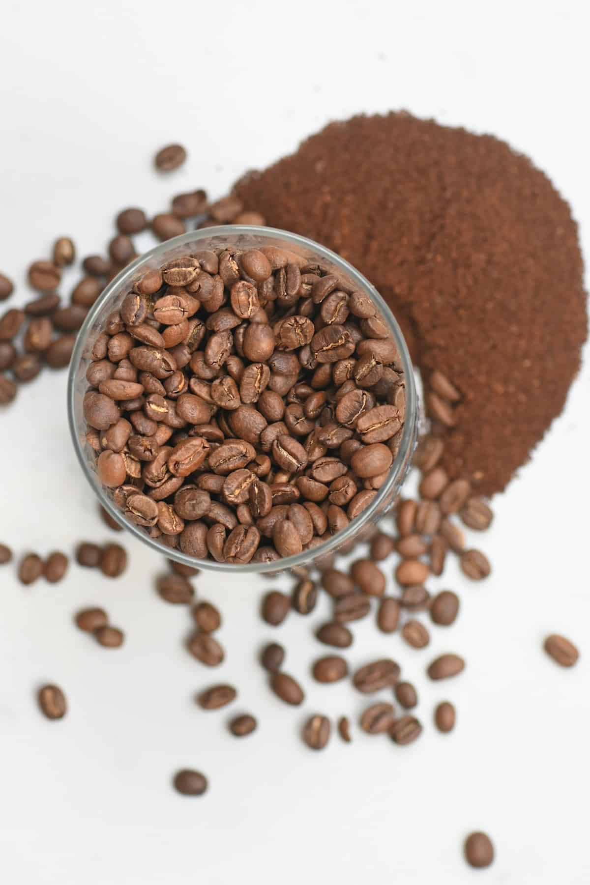 Coffee beans in a container and some ground coffee next to it
