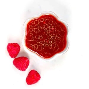 Raspberry Salad Dressing in a small bowl and three raspberries