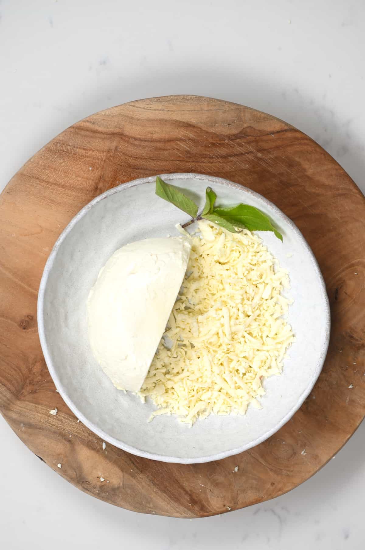 Half-grated mozzarella cheese in a bowl with a mint leaf