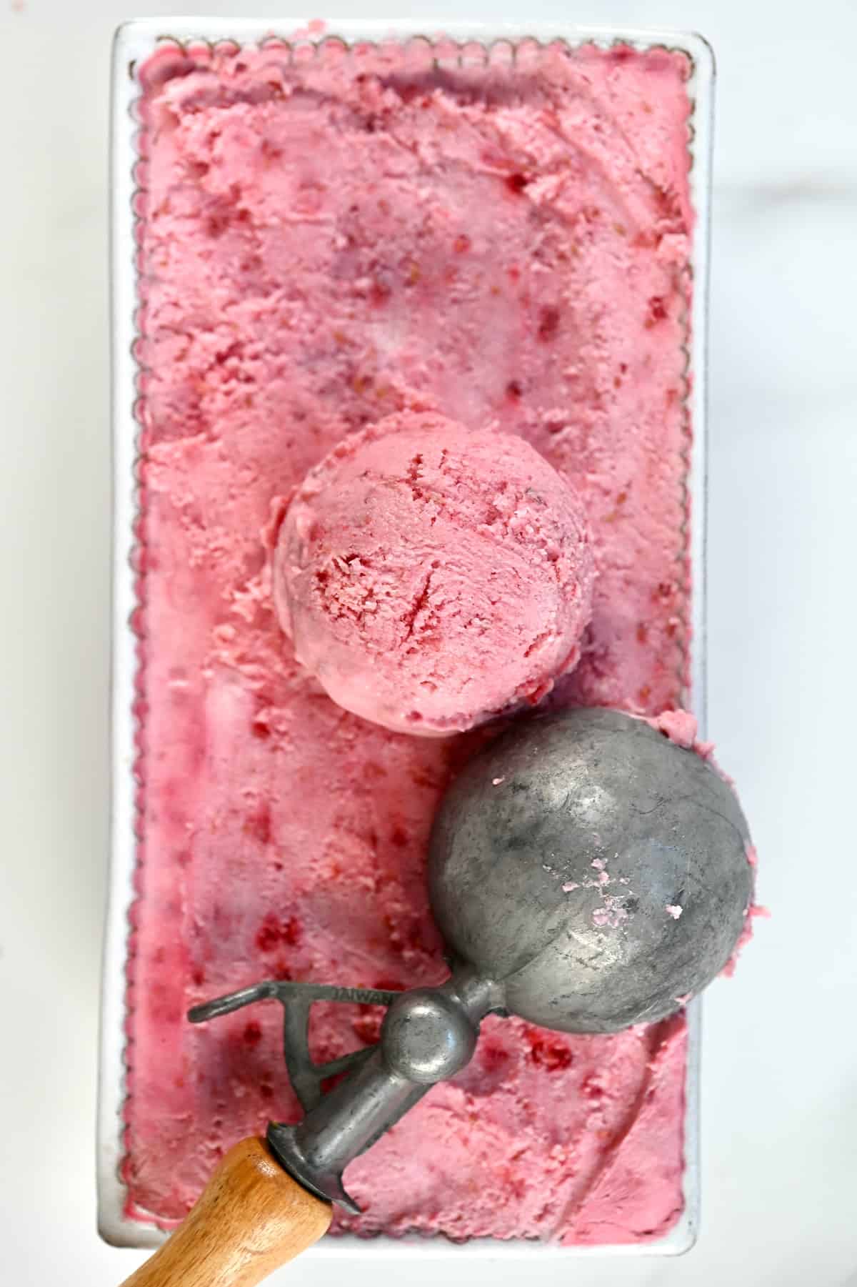 Raspberry Ice Cream in a glass white container with an ice cream scoop