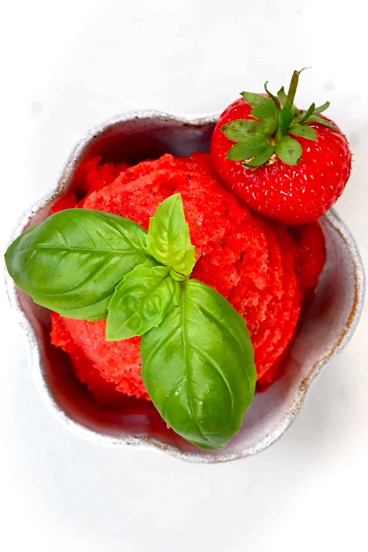 strawberry sorbet scoop inside a cup topped with basil leaf and fresh strawberry