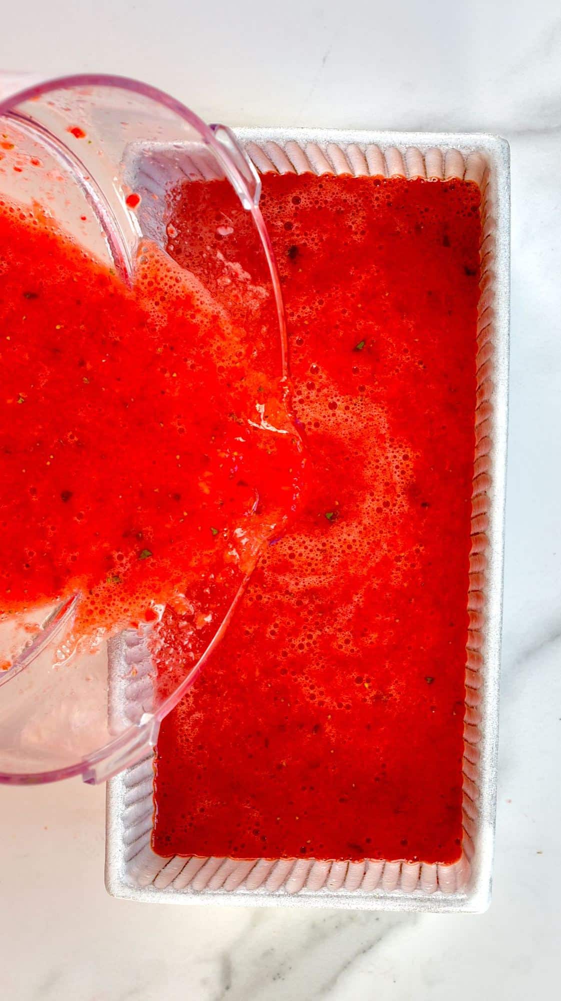 pouring strawberry sorbet mixture into a glass jar