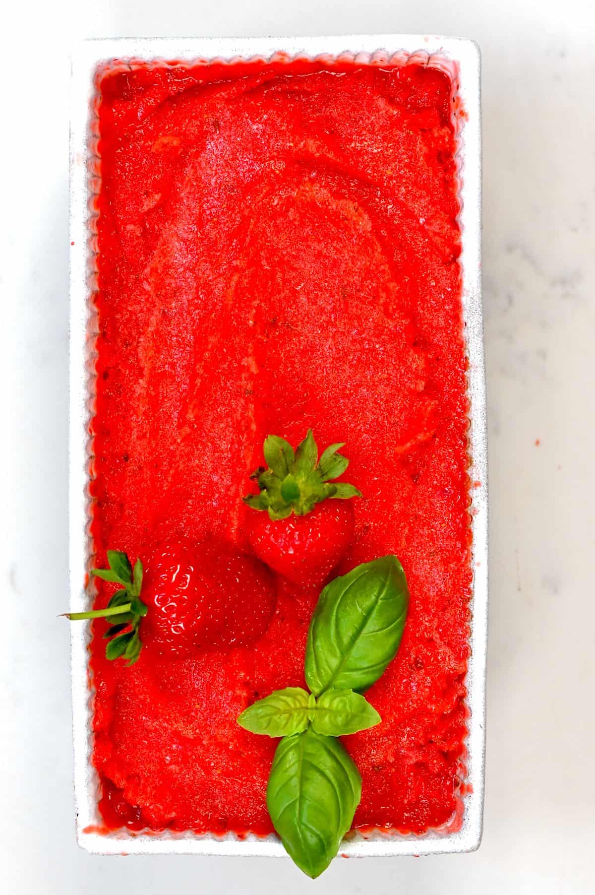 Strawberry Sorbet in a white container decorated with basil leaf and two strawberries