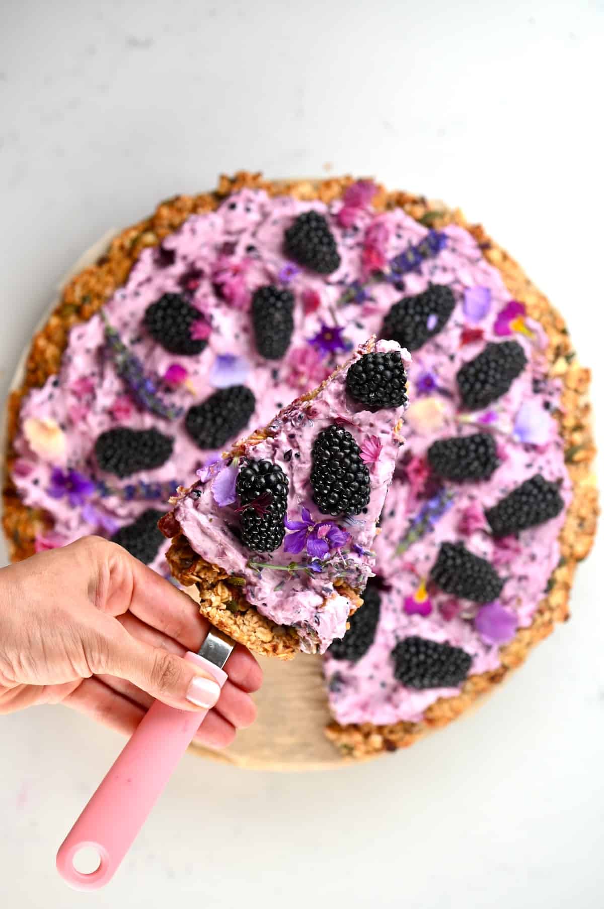 Top view of Blackberry granola pizza with a slice on a spetula