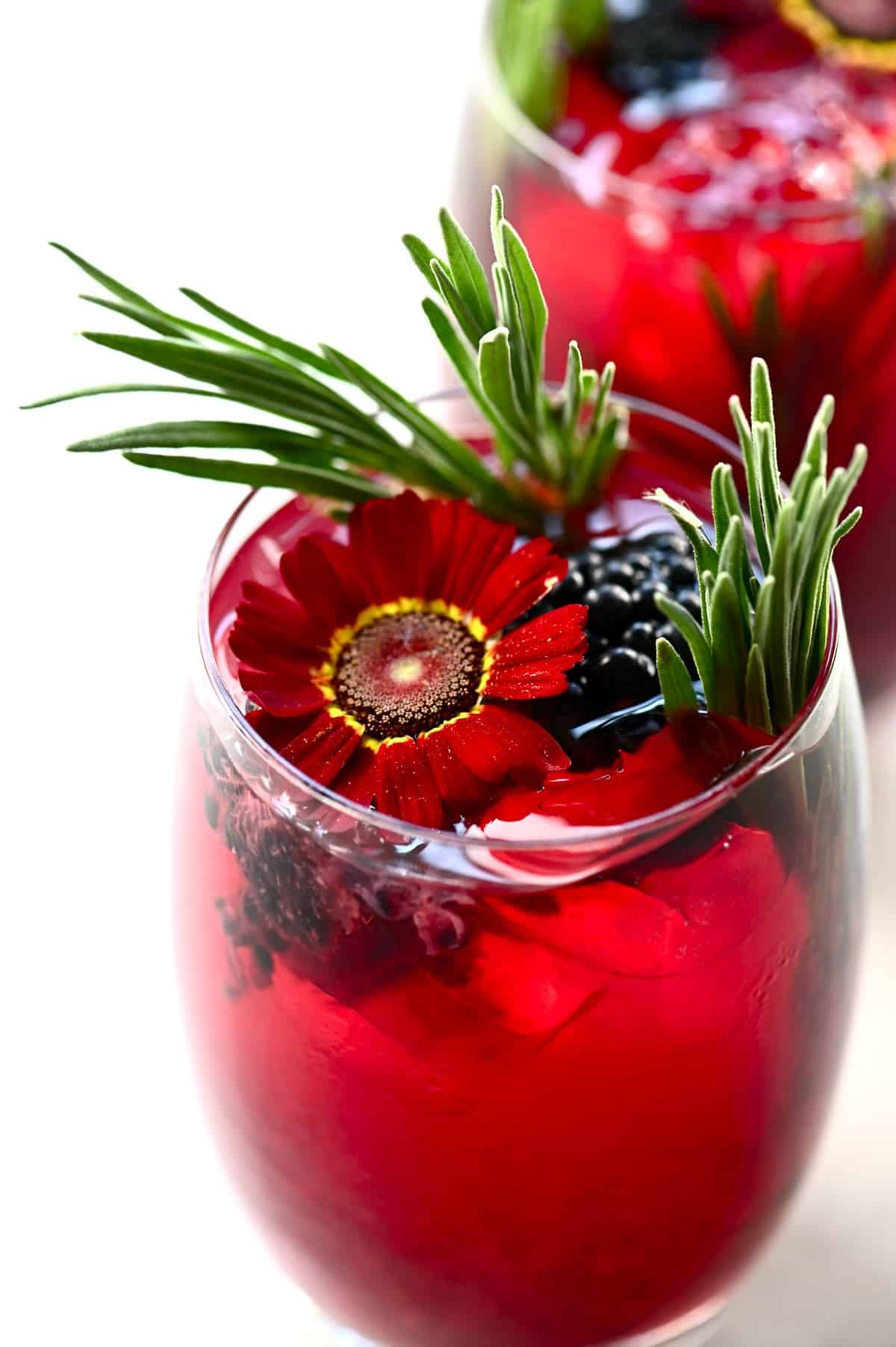 close up of a blackberry iced tea in a glass decorated with edible flowers and herbs