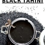A jar with black tahini placed on top of black sesame seeds