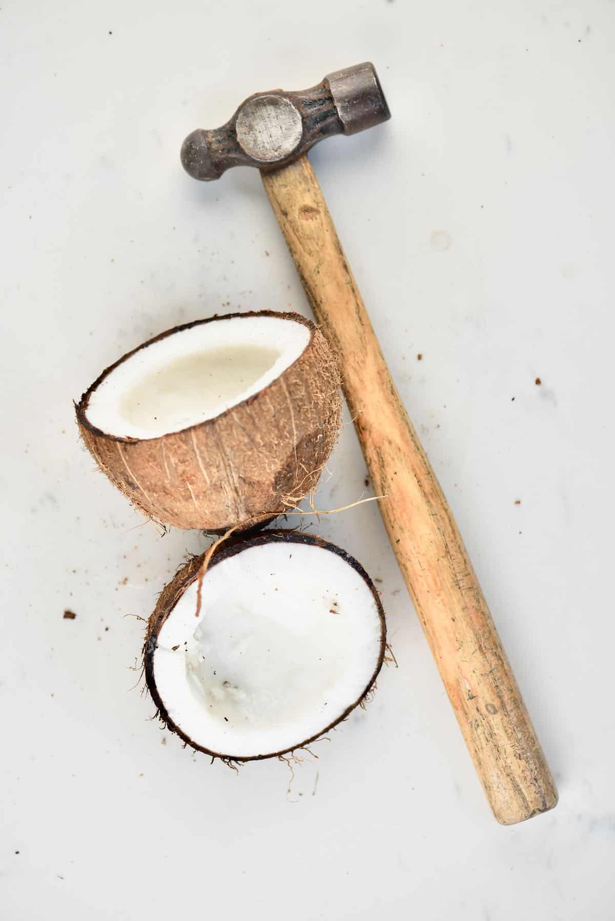 An open coconut and a hammer laying on a flat surface
