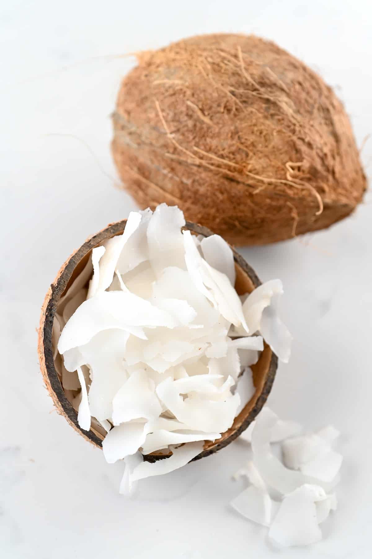 Coconut chips in a small coconut bowl and a whole coconut next to it