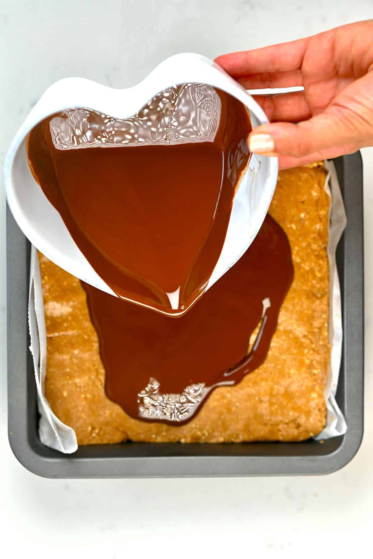 Pouring melted chocolate over peanut butter bars