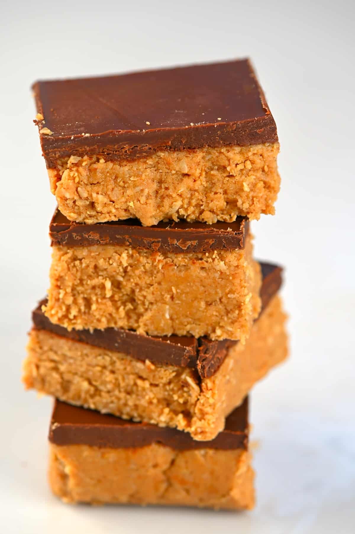 Four peanut butter bars with chocolate coating stacked on top of each other