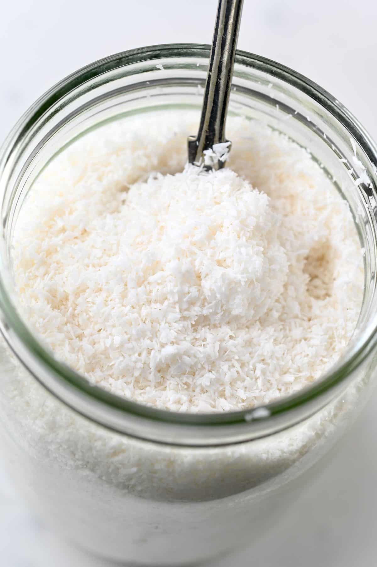 An open jar with Shredded Coconut and a spoon dipped in it