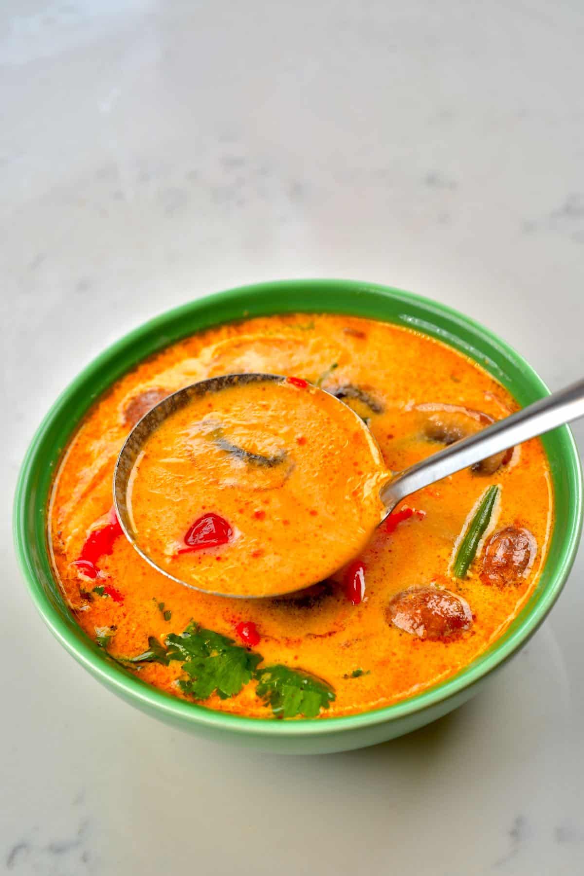 A ladle with tom yum soup filling up a green bowl