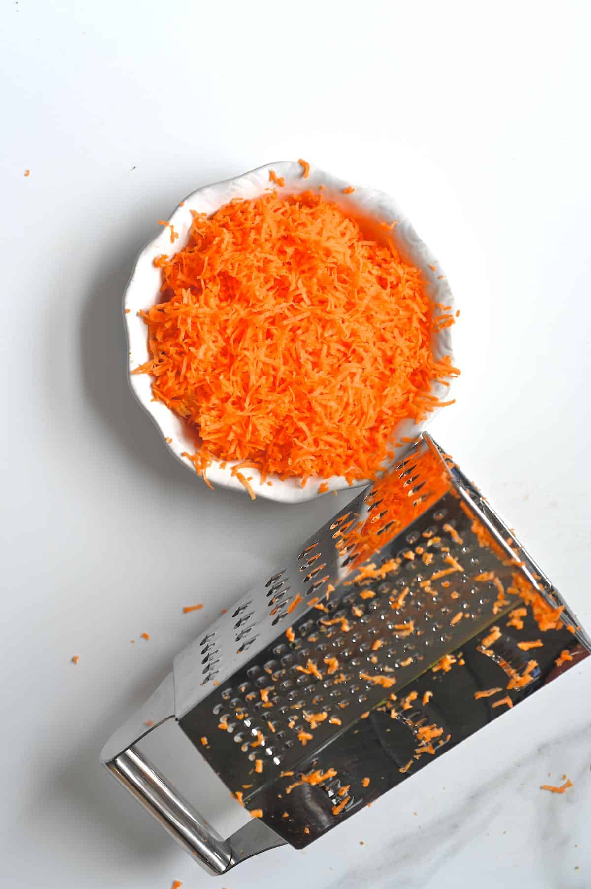 Crated carrots in a small dish and a grater next to it