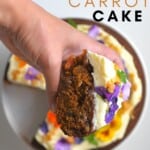A slice of carrot cake being held above the cake